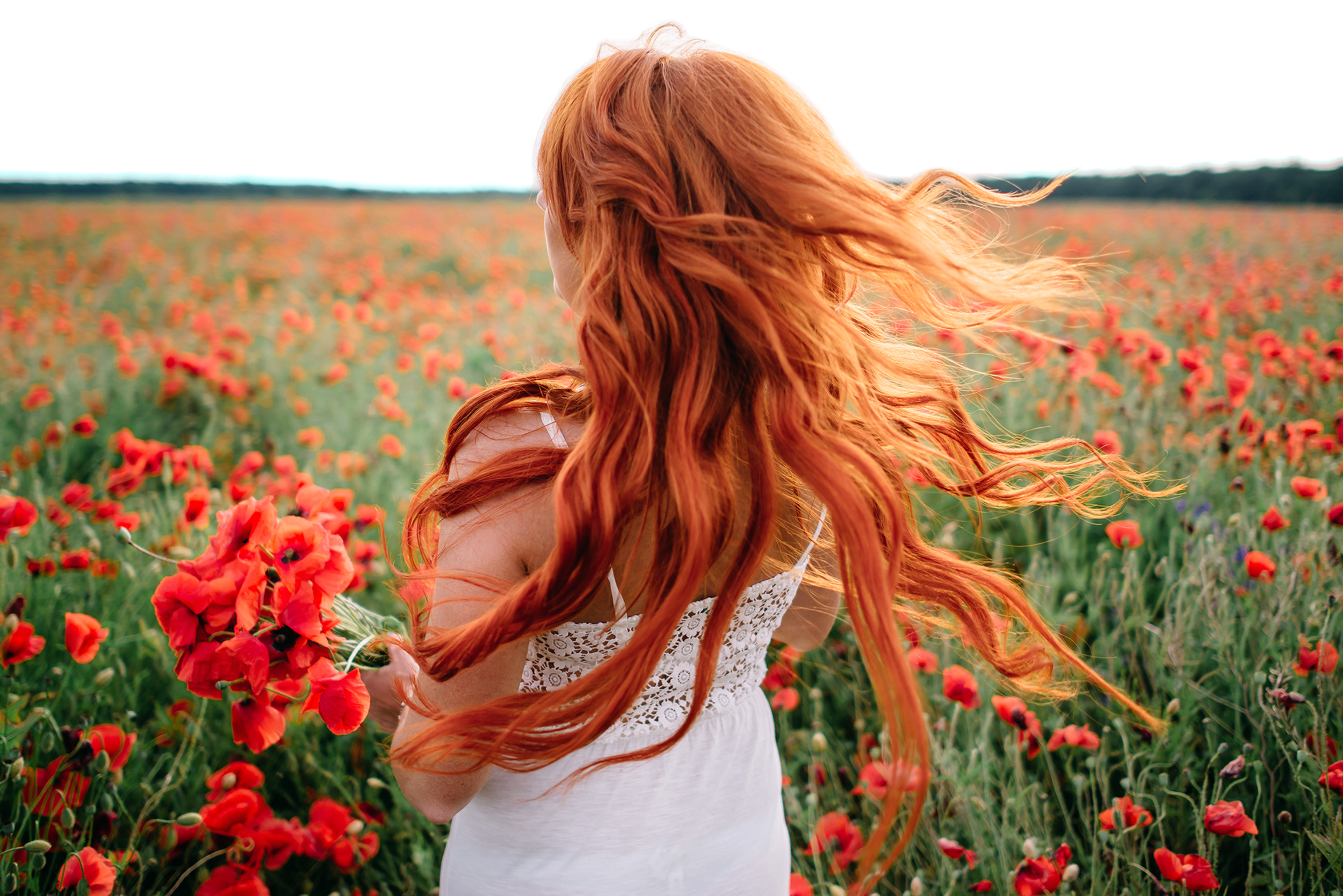 Beautiful young red-haired woman in poppy field with flying hair - Sentirna...