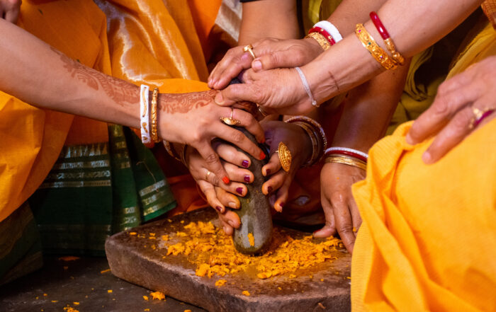 Group Of Indian Women Holding A Stone Peace Of Mortar For Making Turmeric Paste For Wedding Ceremony. Its A Rituals Of Traditional Hindu Wedding Which Is Known As Haldi Ceremony.